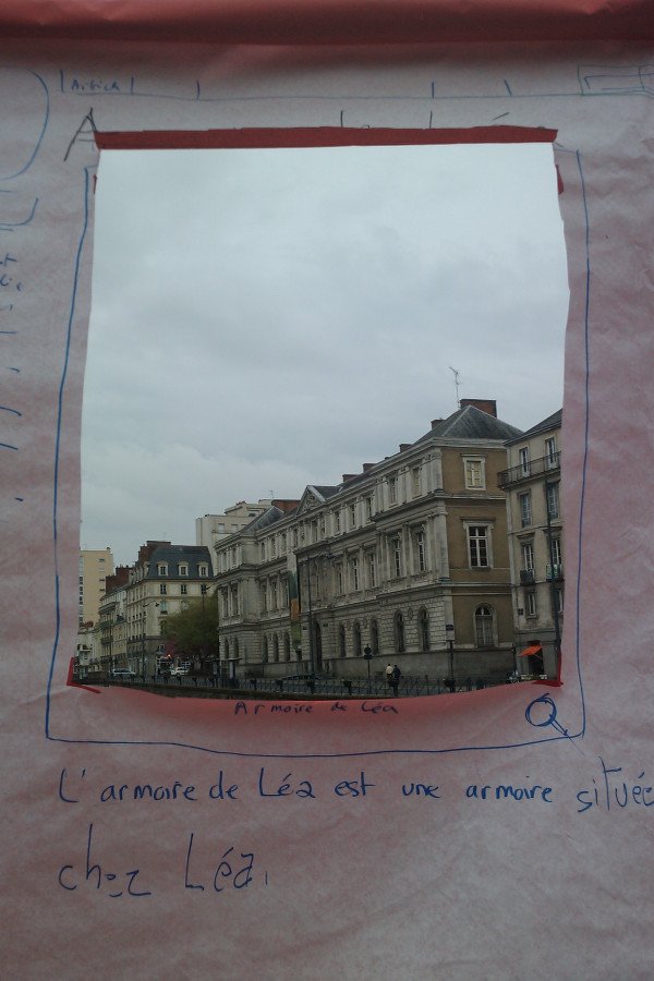 Vue du musée des beaux-arts de Rennes au travers d'une fenêtre découpée dans une nappe en papier, sous laquelle est écrit "L'armoire de Léa est une armoire située chez Léa".