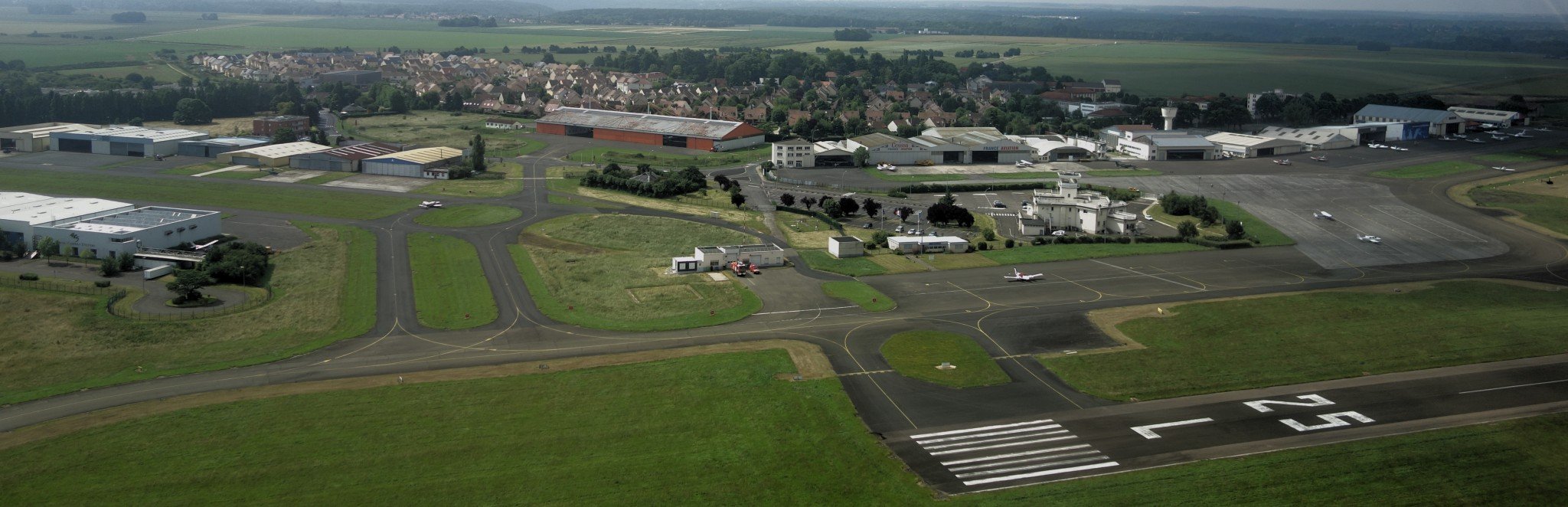 Une tour de contrôle et des hangars au bord de pistes, dont une de décollage marquée "25 L".