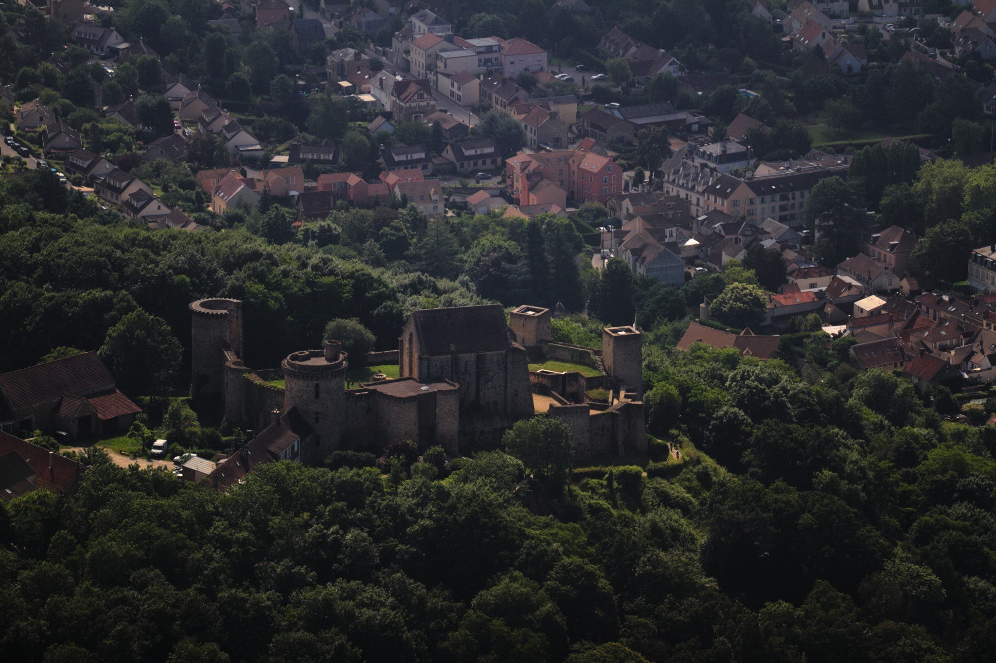 Un château fort en pierre au milieu de la végétation, sur une hauteur surplombant une petite ville.