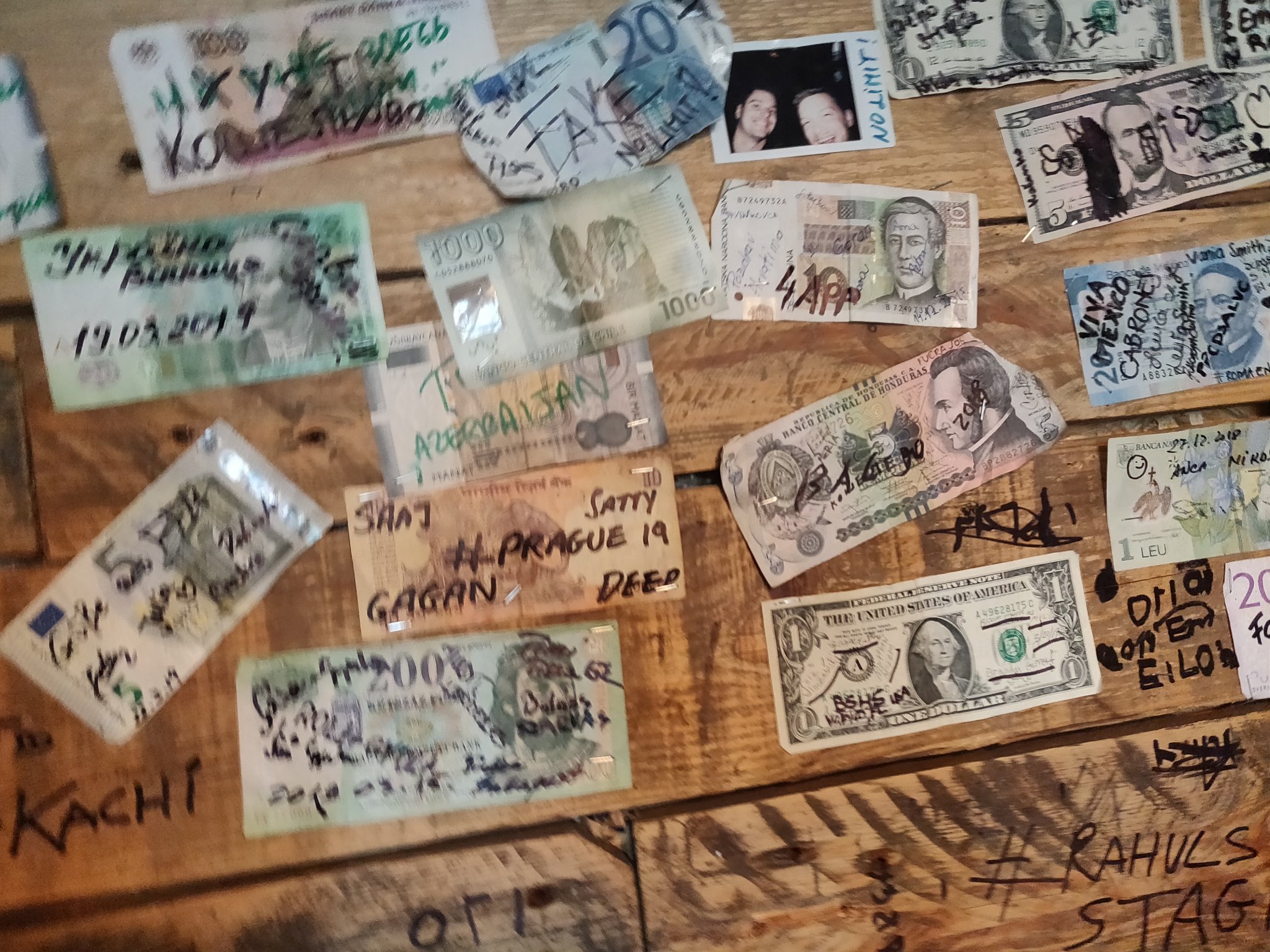 Des billets de banque collés sur une paroi en bois, et sur lesquels des petits mots ont été écrits au feutre.