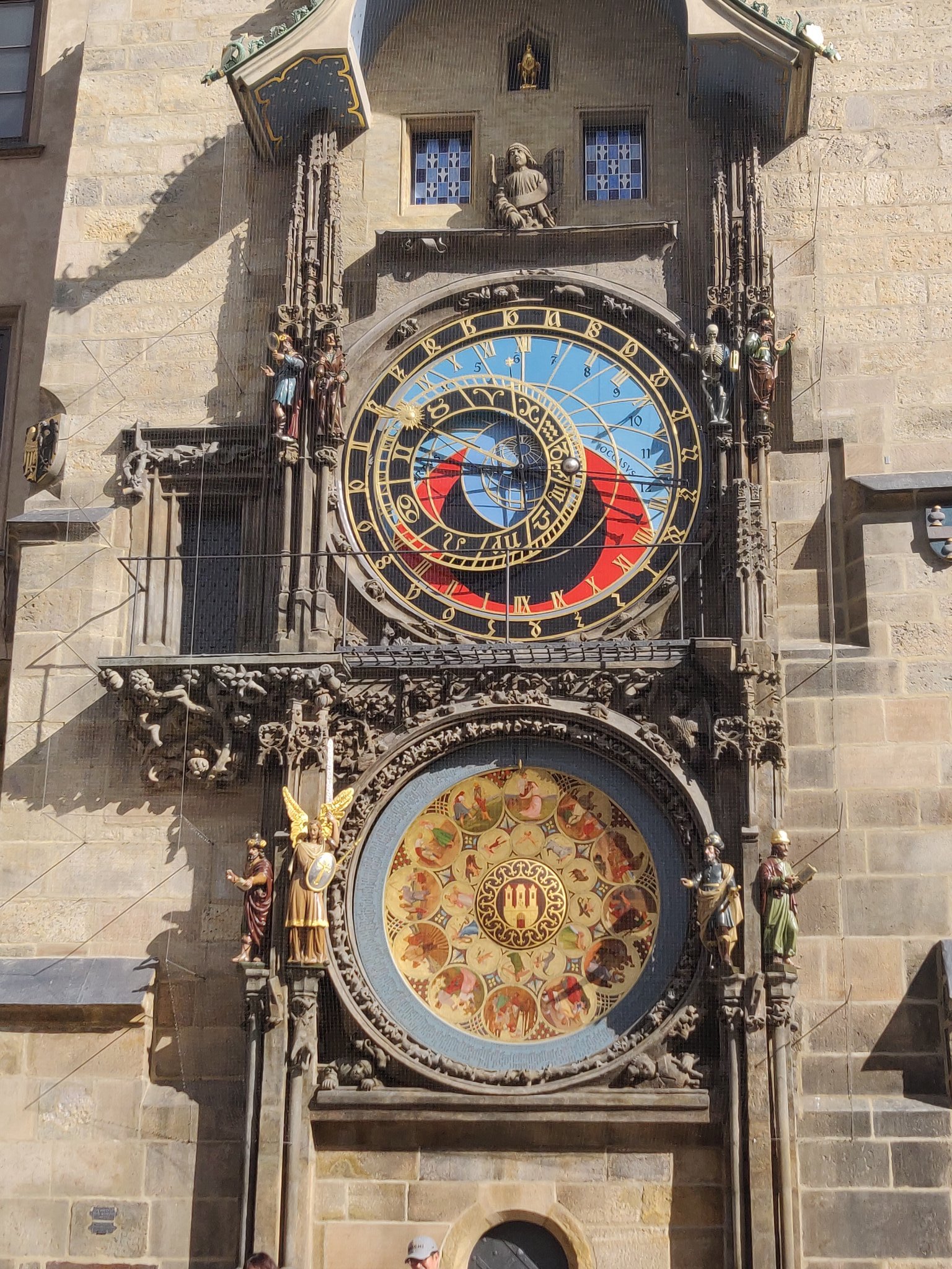 Une horloge astronomique du 15e siècle. Elle est chargée de nombreux cadrans noirs à chiffres dorés, indiquant la position du soleil et de certains astres. Le fond principal est bleu et rouge.