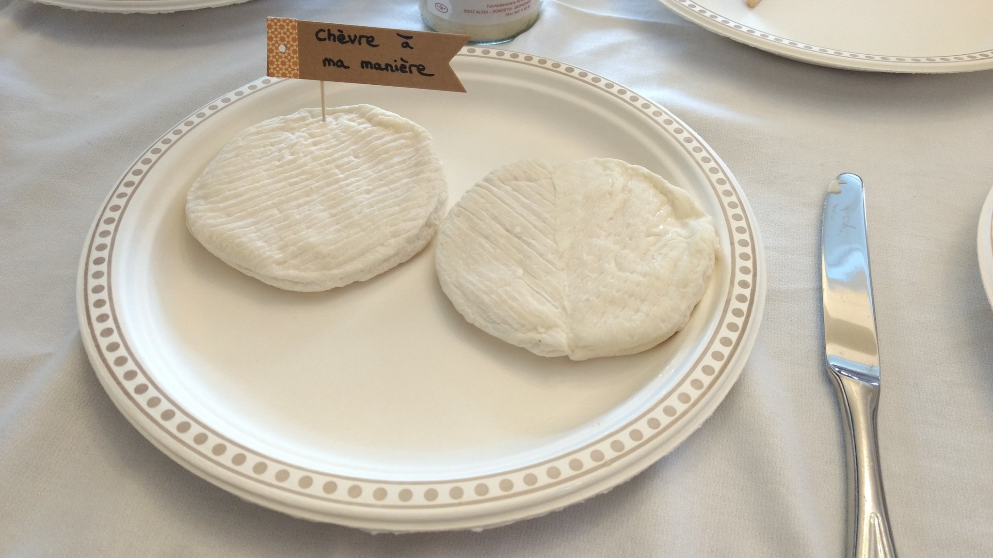 Deux fromages de chèvres dans une assiette, avec un petit drapeau indiquant "Chèvre à ma manière" planté dedans.