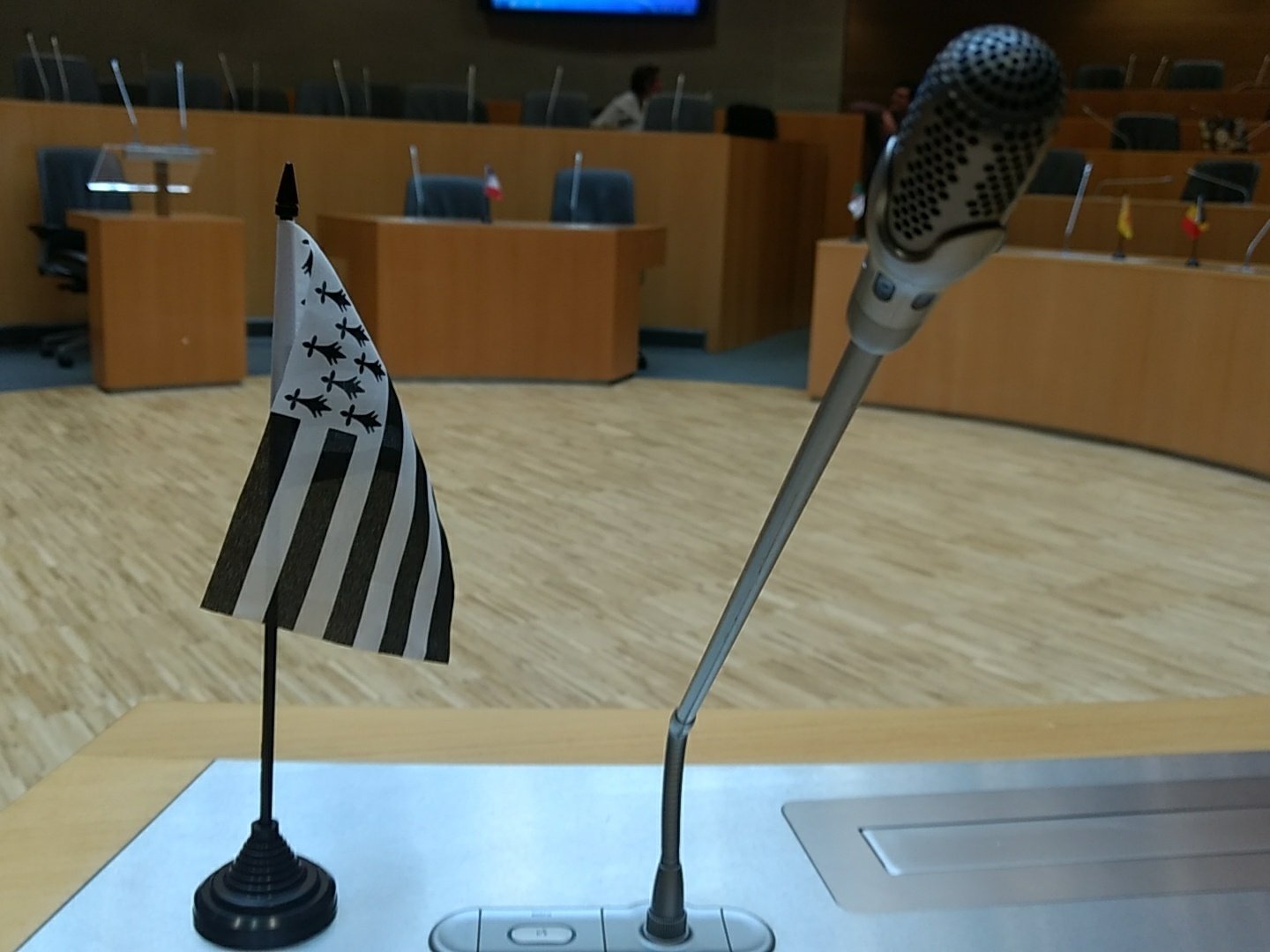 Un petit drapeau posé sur un pupitre à côté d'un micro dans une salle de conférence, façon sommet de l'ONU