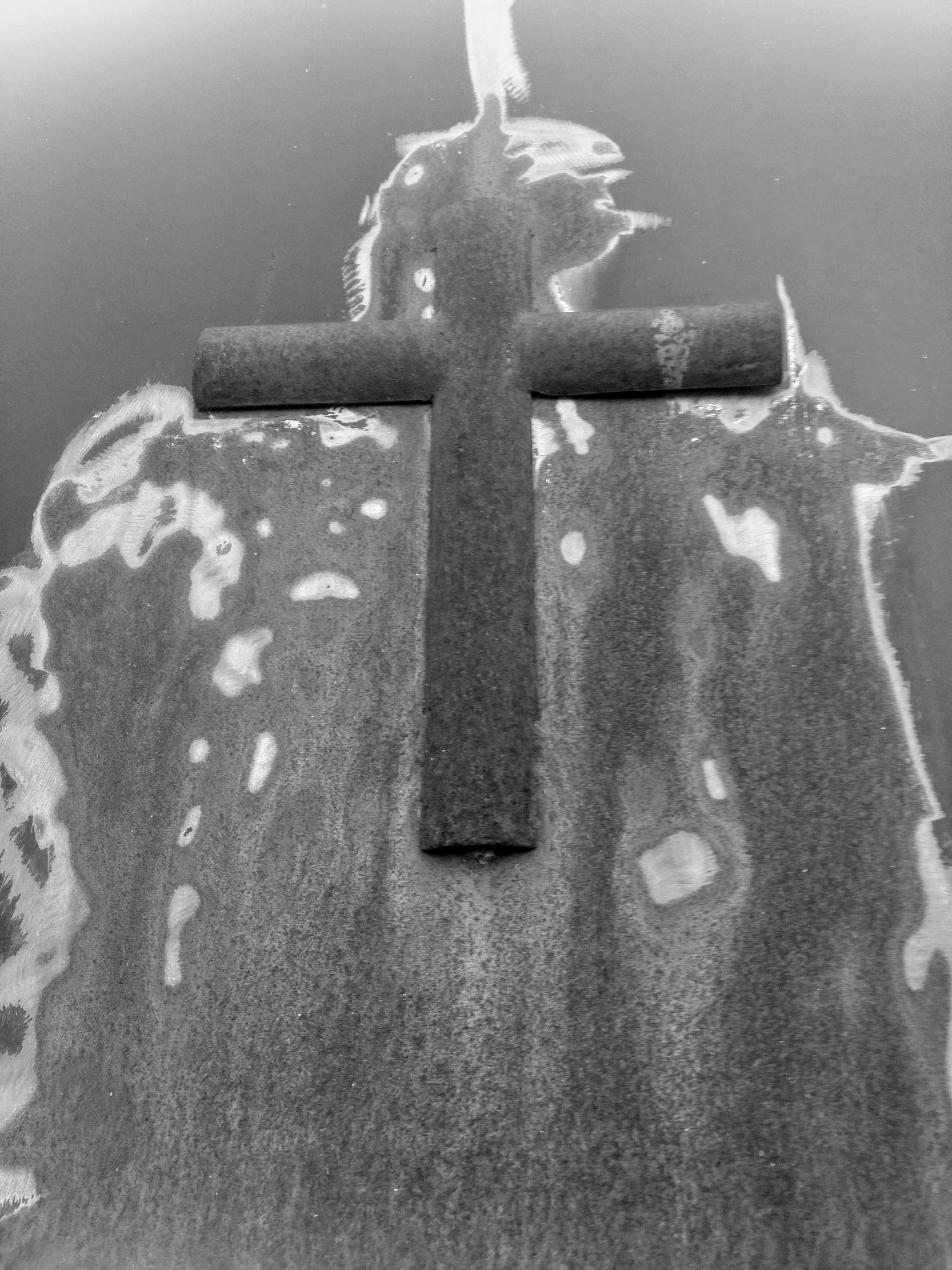 Un crucifix en fer sur une porte en métal rouillée.