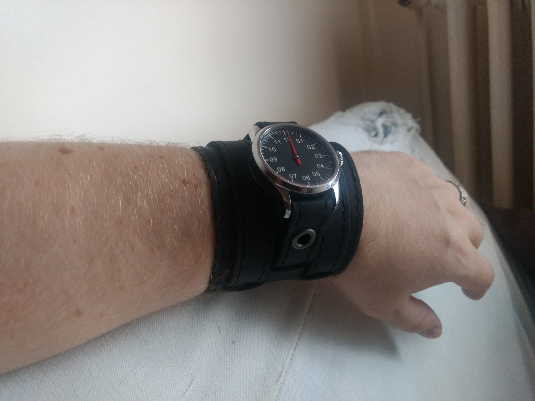 Montre monoaiguille noire avec un bracelet très large, portée au poignet.