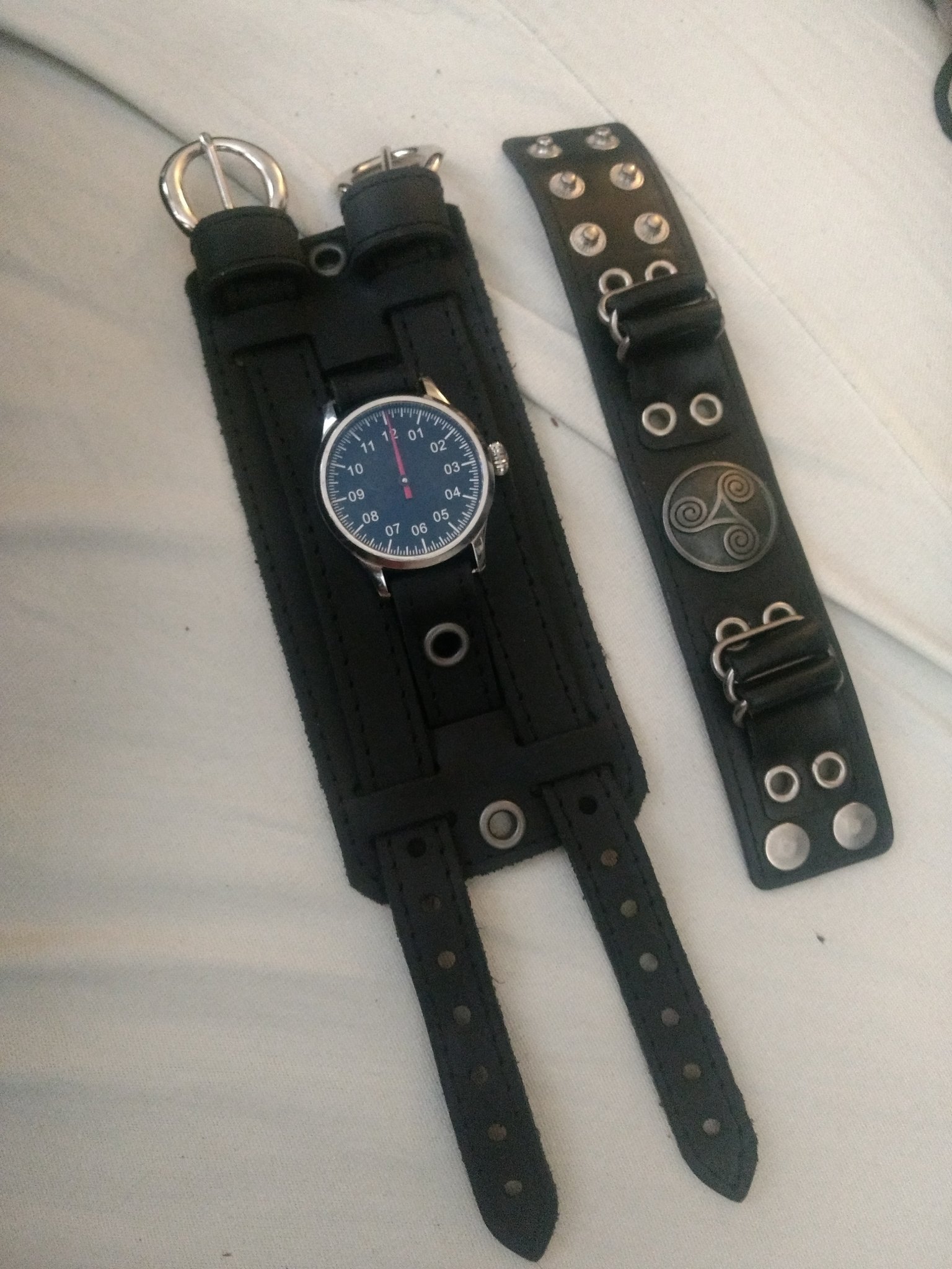 La montre est posée sur un drap à côté d’un bracelet de force qui paraît minuscule à côté