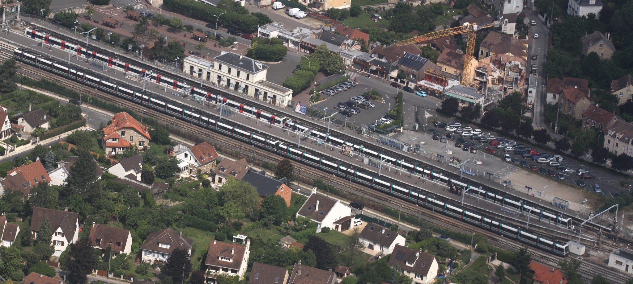 Un bâtiment de gare blanc assez classique pour une gare RER, le long de voies de chemin de fer qui traversent la photo en diagonale.