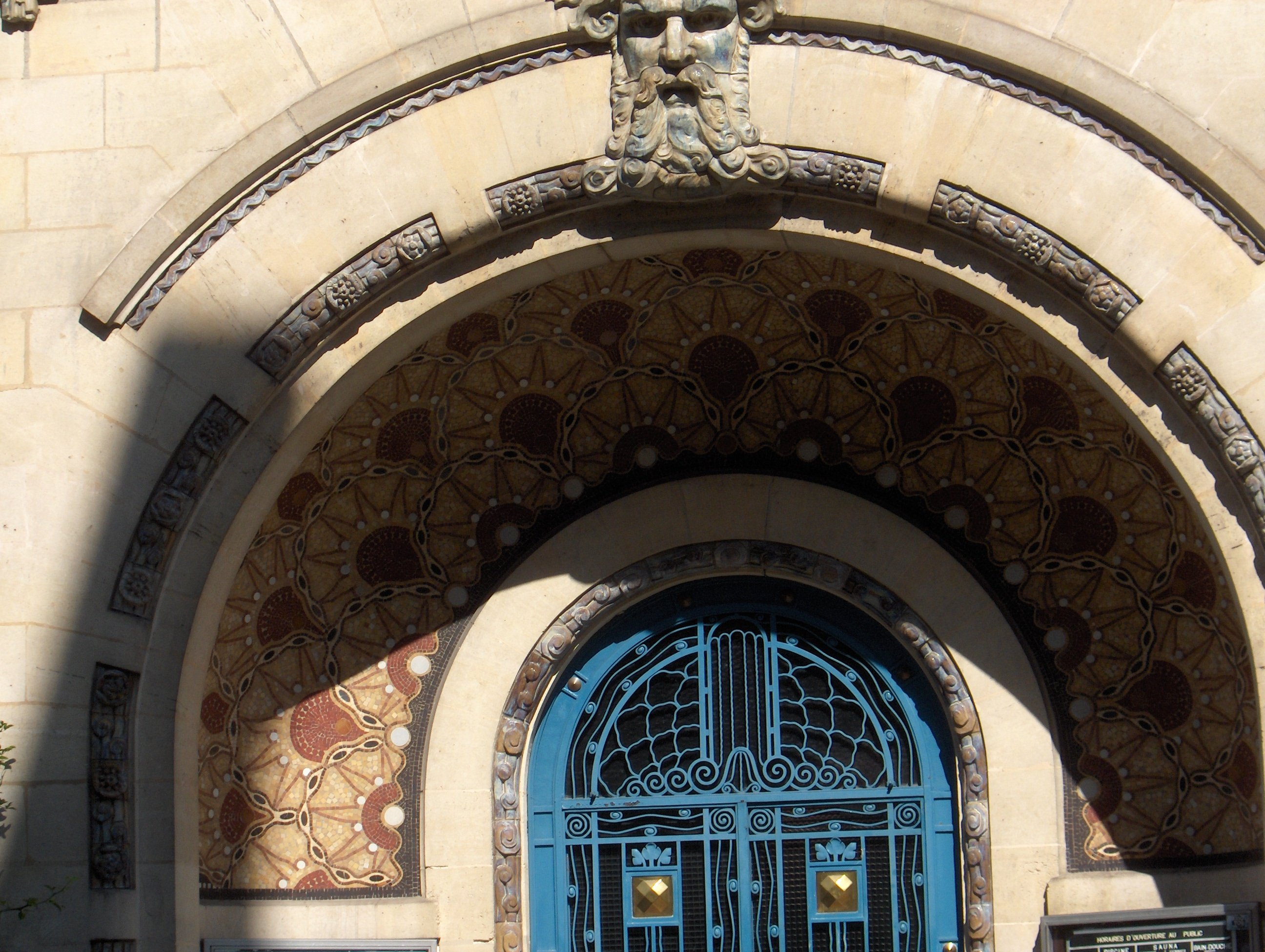 Entrée art déco avec une mosaïque à motifs géométriques ocres disposés en alcôve autour de la porte principale, bleue.