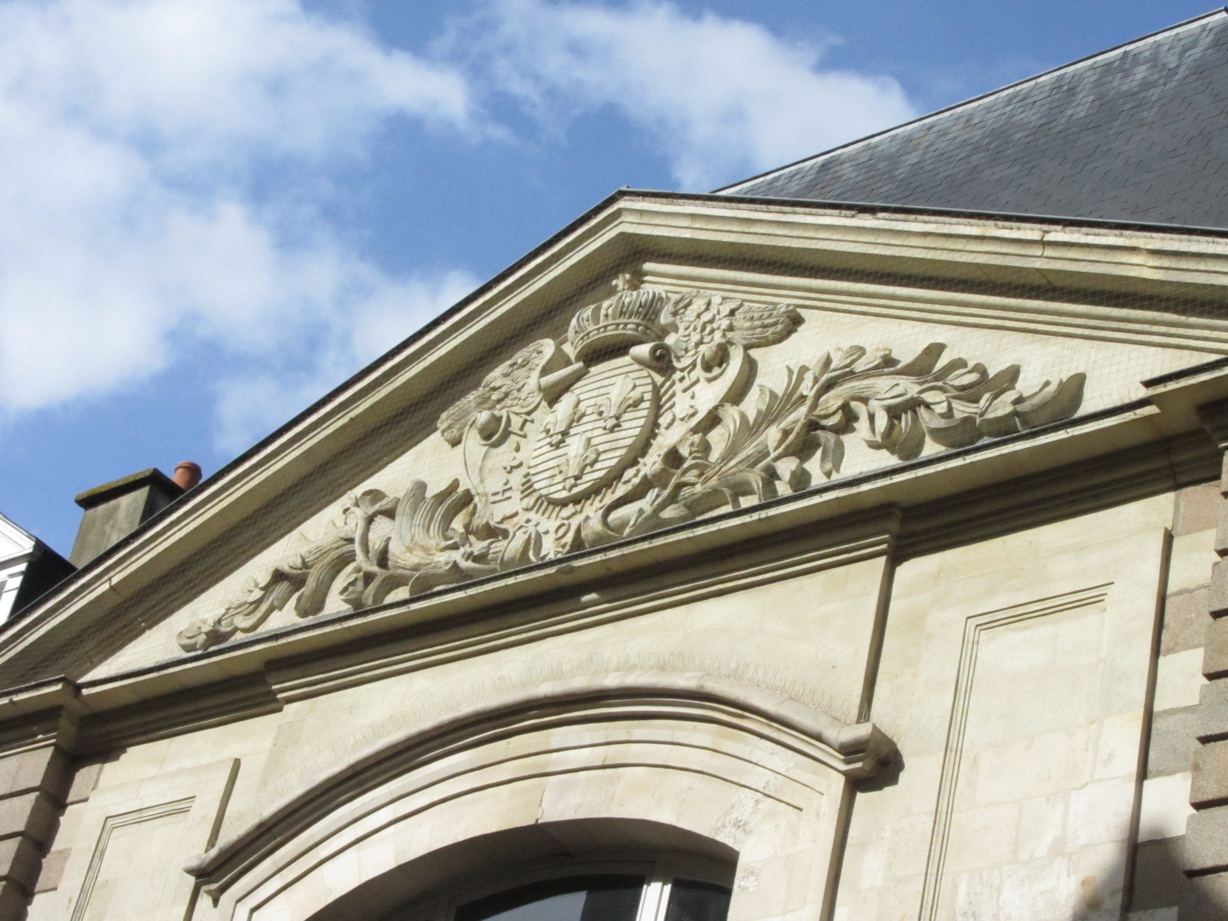 Bas relief avec les armoiries de la France (d'azur aux trois fleurs de lys d'or) sur le fronton d'un bâtiment.