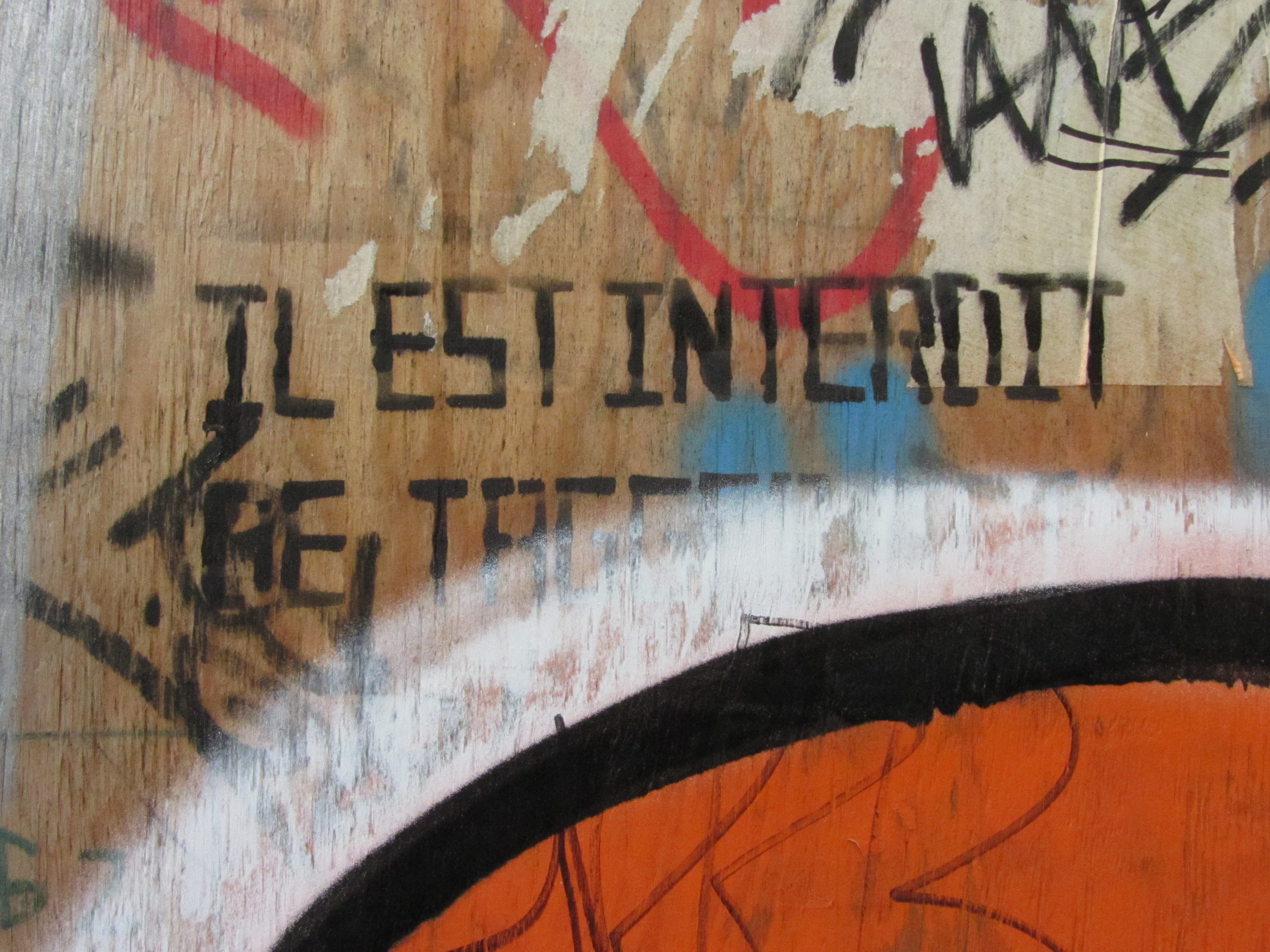 Panneau en bois sur lequel la mention "Il est interdit de tagguer" est peinte au pochoir et à moitié recouverte de tags.