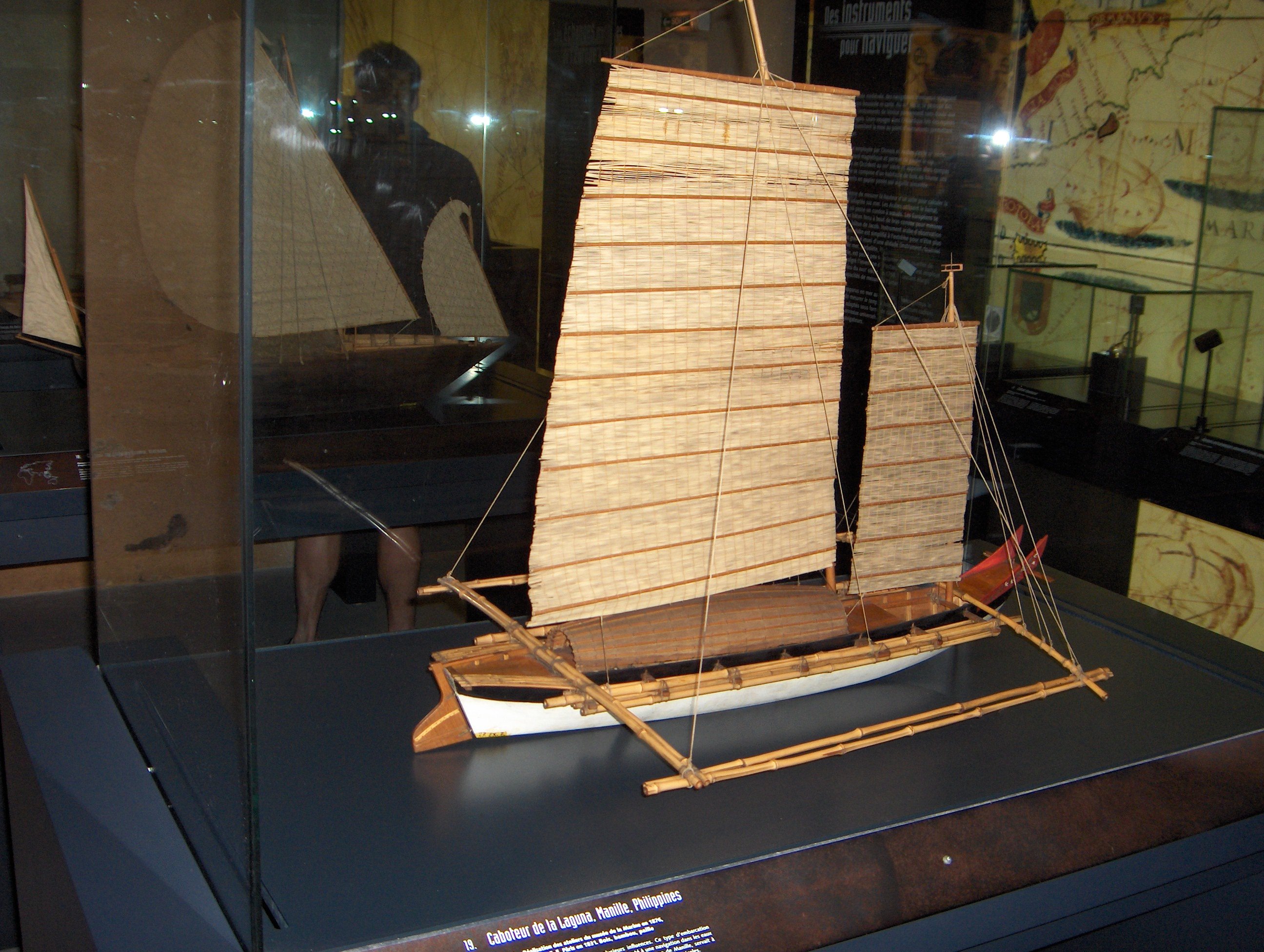 Une maquette de bateau avec deux voiles carrées et des balanciers latéraux en bambou