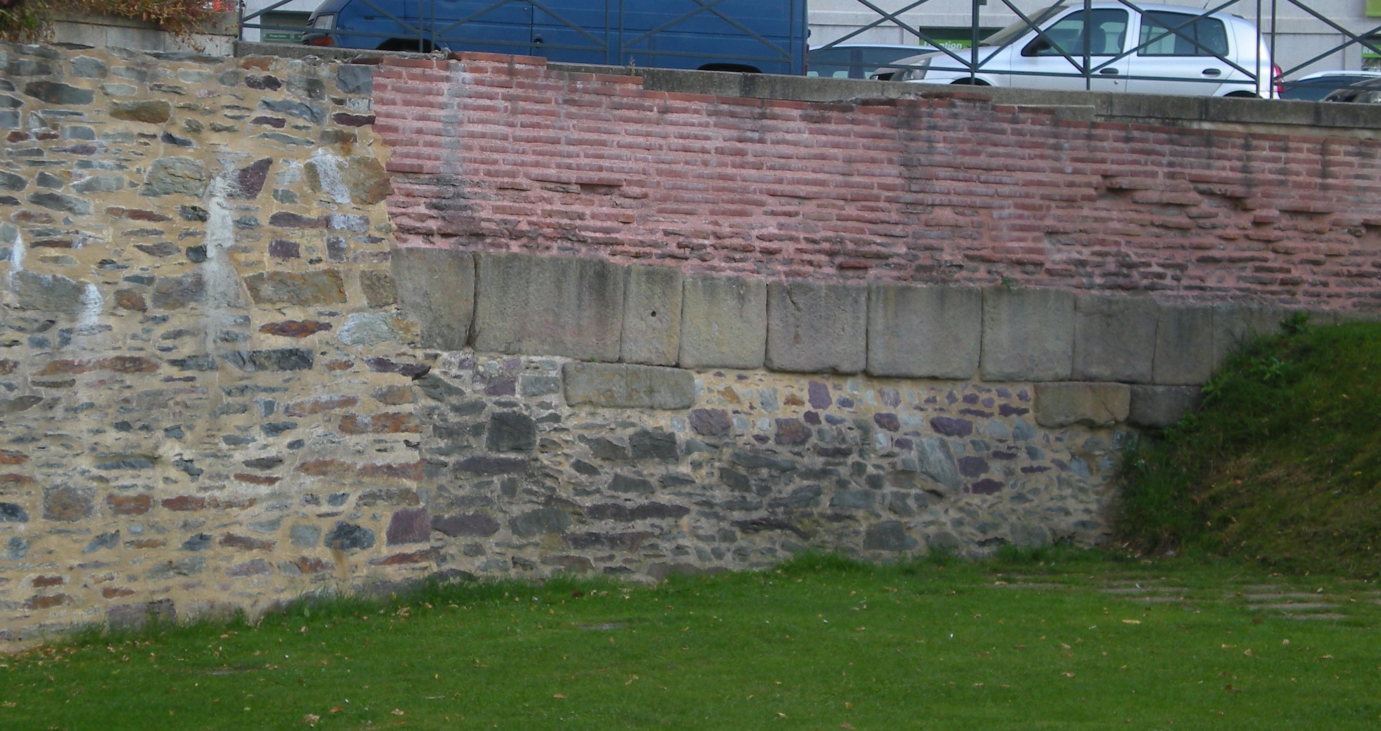 Un mur de pierres médiéval dont une partie a été retirée, montrant un mur de briques rouges derrière.
