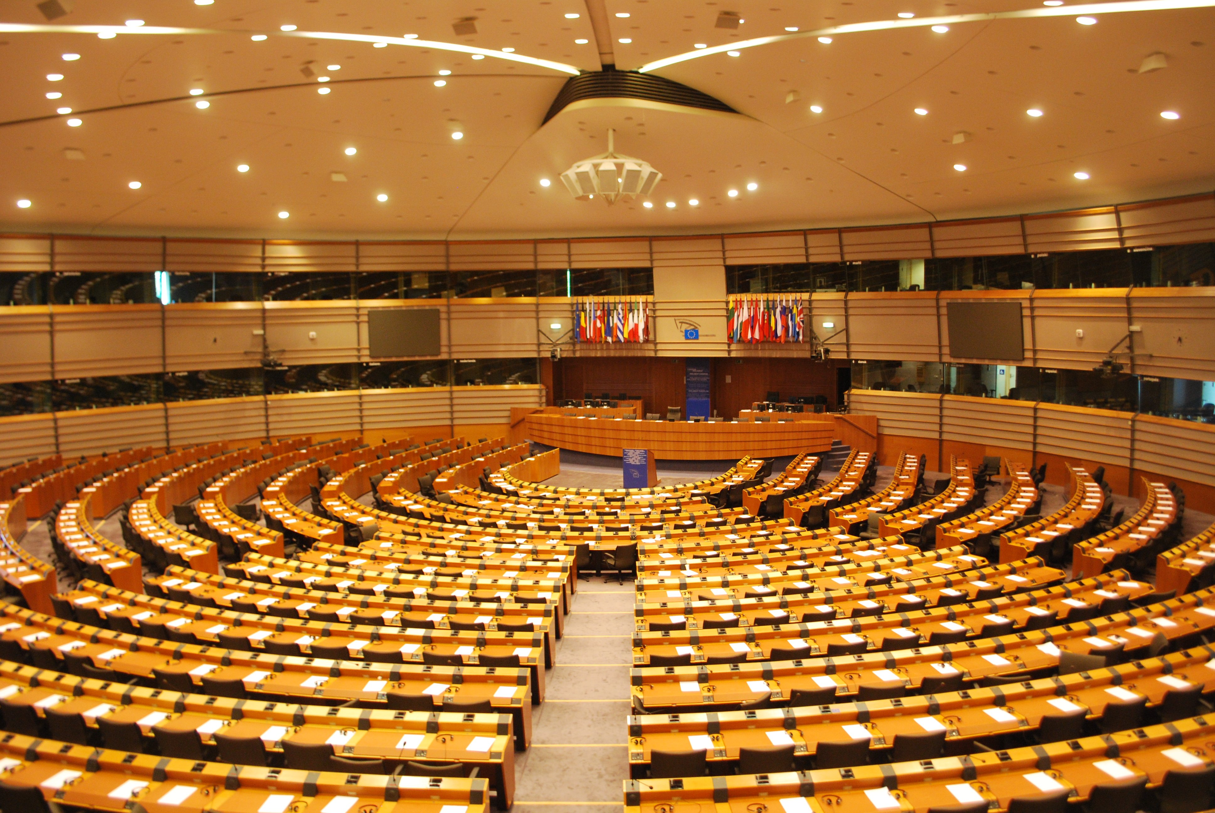 Une très grande salle avec des pupitres disposés en arcs de cercle concentriques, et un podium au milieu, et derrière ce podium un grand bureau surmonté de drapeaux.