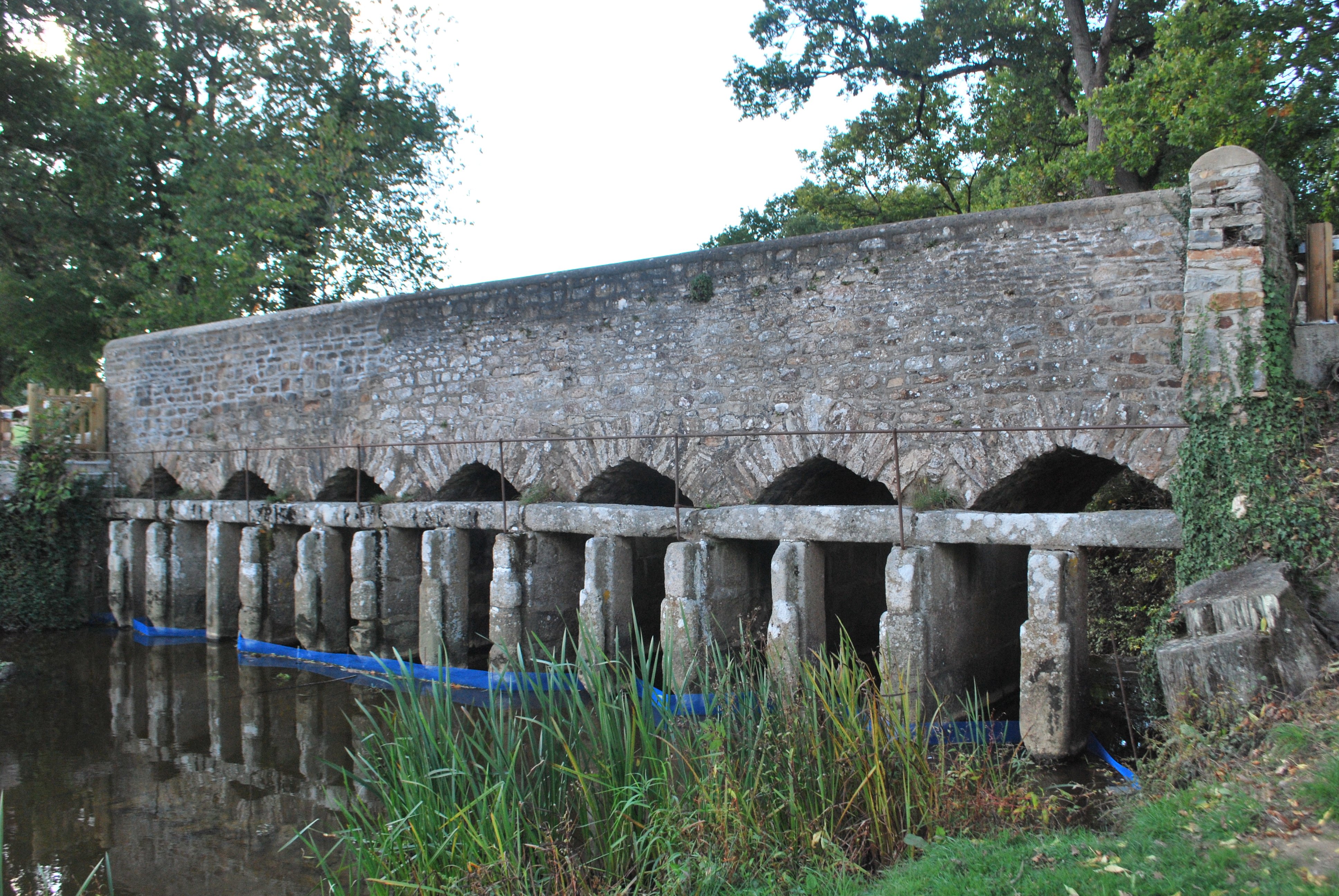 Un pont en pierre avec plusieurs arches. On voit juste devant des encoches pour mettre des panneaux en bois, servant à fermer le bassin longé par le pont.