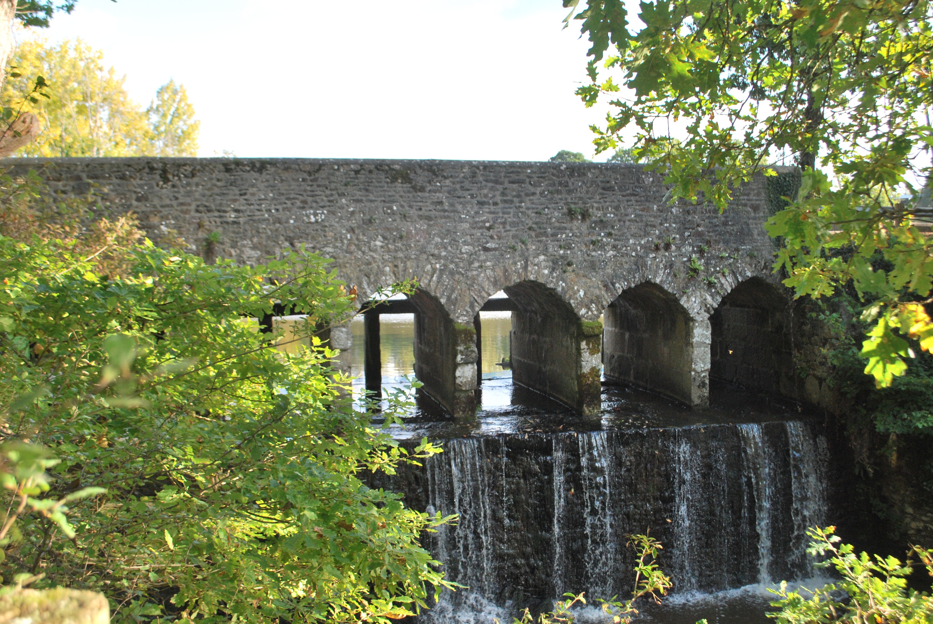 Un pont en pierre avec plusieurs arches, le long d'une chute d'eau artificielle. On devine des encoches pour mettre des panneaux en bois de l'autre côté, servant à fermer le bassin longé par le pont.