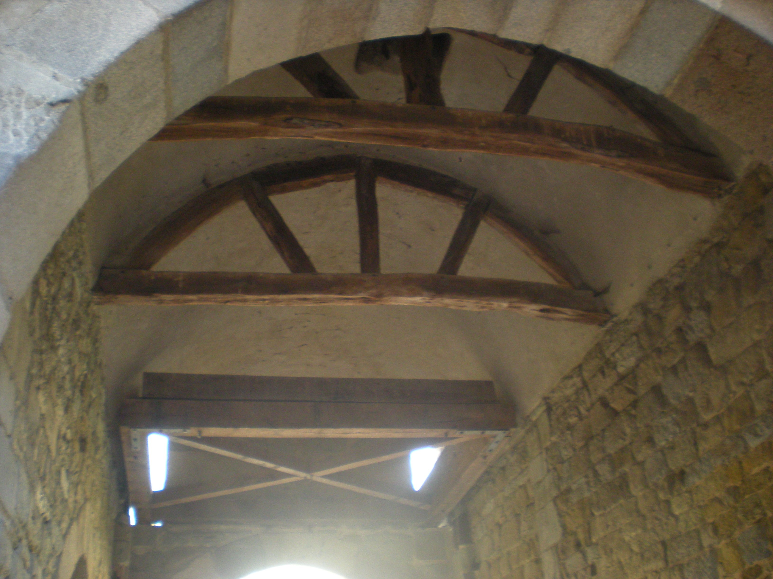 Vue d'une voûte entre deux murs en pierre, renforcée par des structures en bois.
