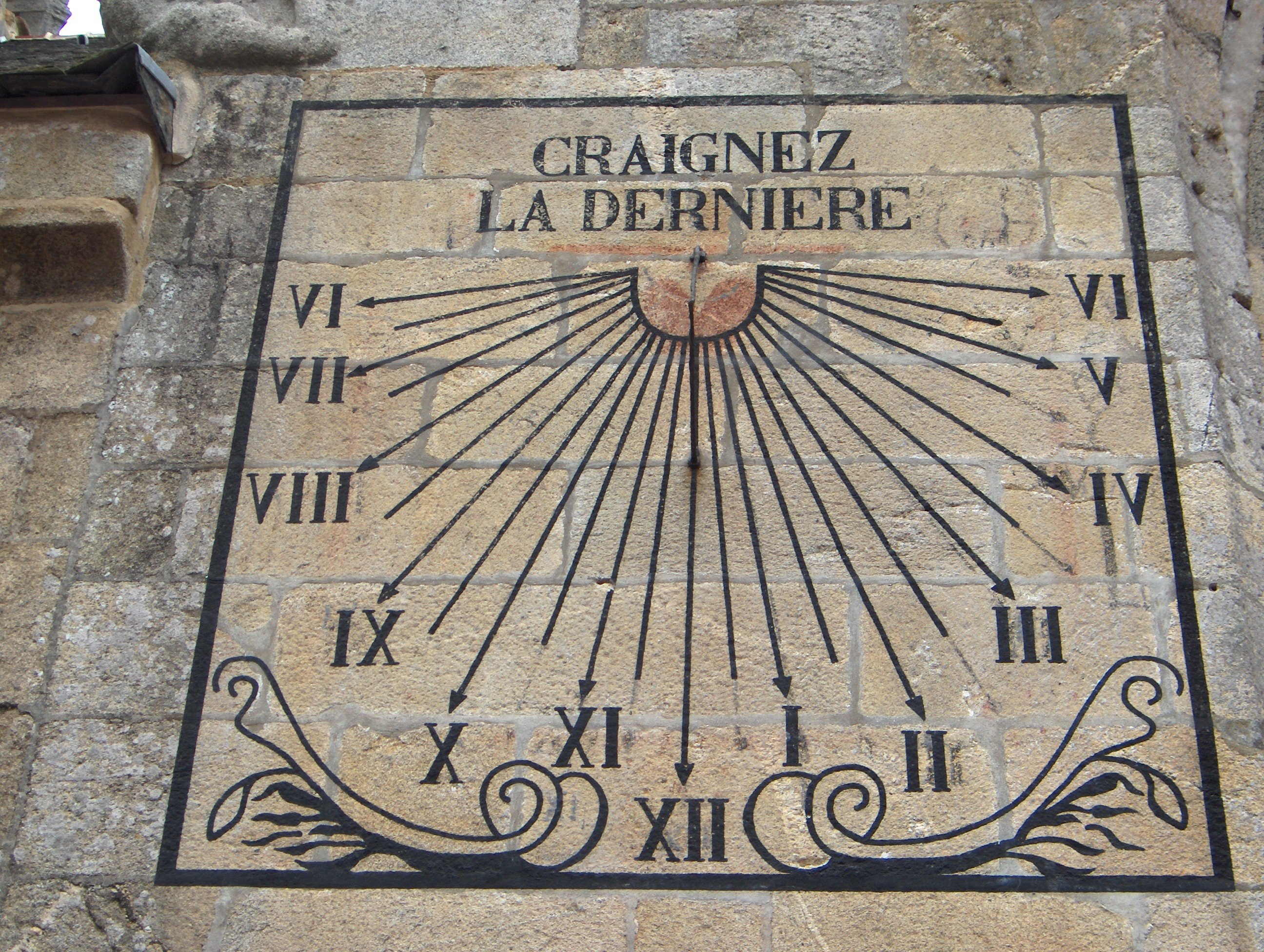 Un cadran solaire peint sur le mur d’une église, surmonté de l’inscription « Craignez la dernière »