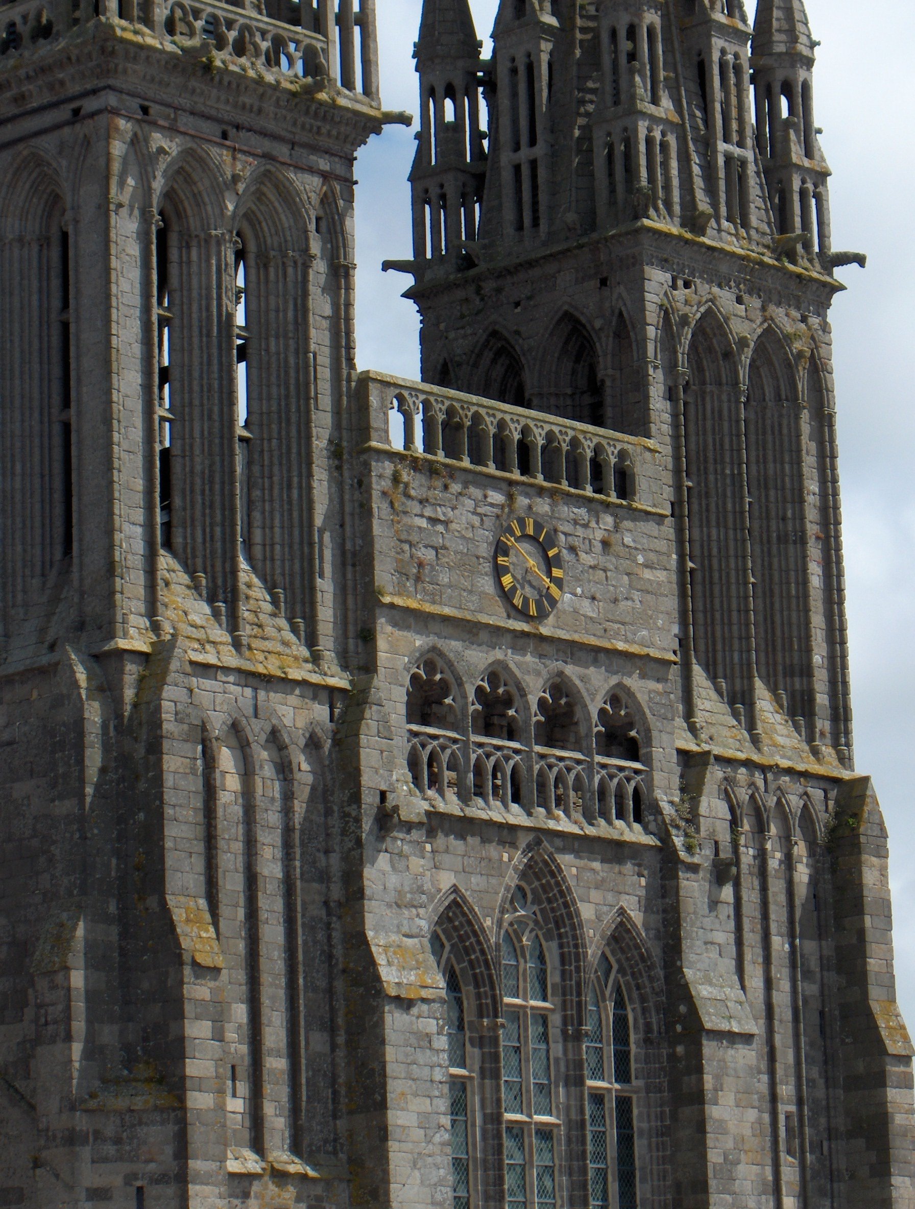 Façade d'une cathédrale gothique en granit, avec une horloge noire à chiffres et aiguilles dorés
