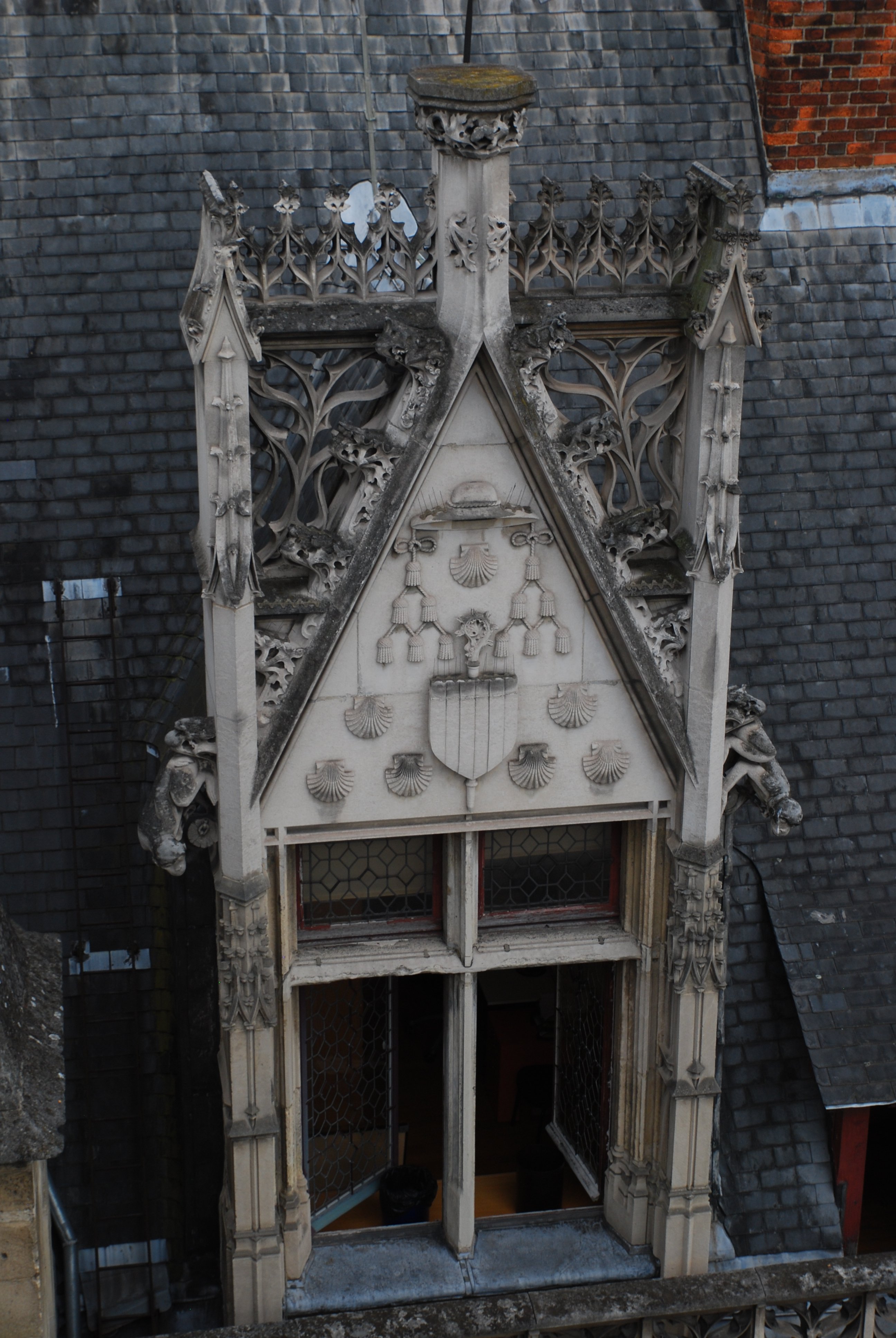 Encadrement de fenêtre de l’hôtel de Cluny au niveau des toits. Elles est surmontée d'un fronton triangulaire en pierre où figure un écu palé surmonté d’un chapeau d’évêque et entouré par des coquilles Saint-Jacques. Les bords supérieurs du fronton portent des motifs de feuille de houx, et des grotesques émergent des montants verticaux sur les côtés. La fenêtre elle-même est divisée en quatre par des meneaux en pierre en forme de croix latine.
