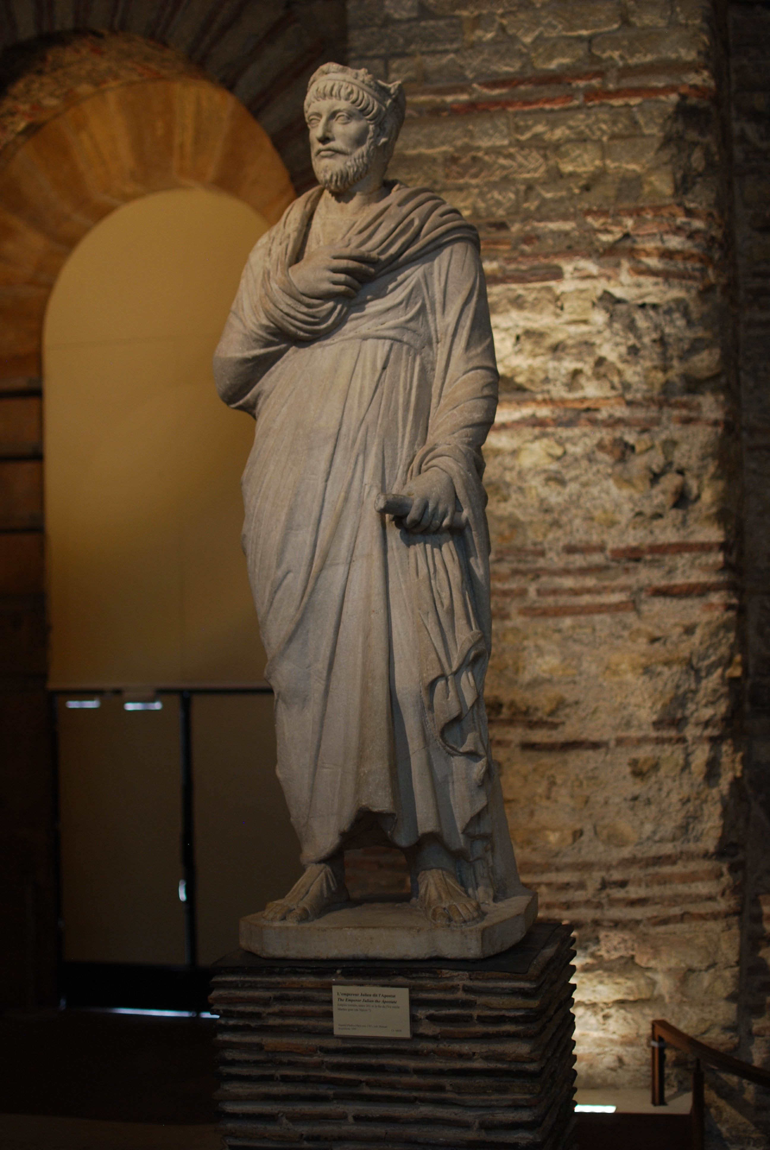 Statue en pied d'un homme, portant une robe et tenant un petit bâton dans la main.
