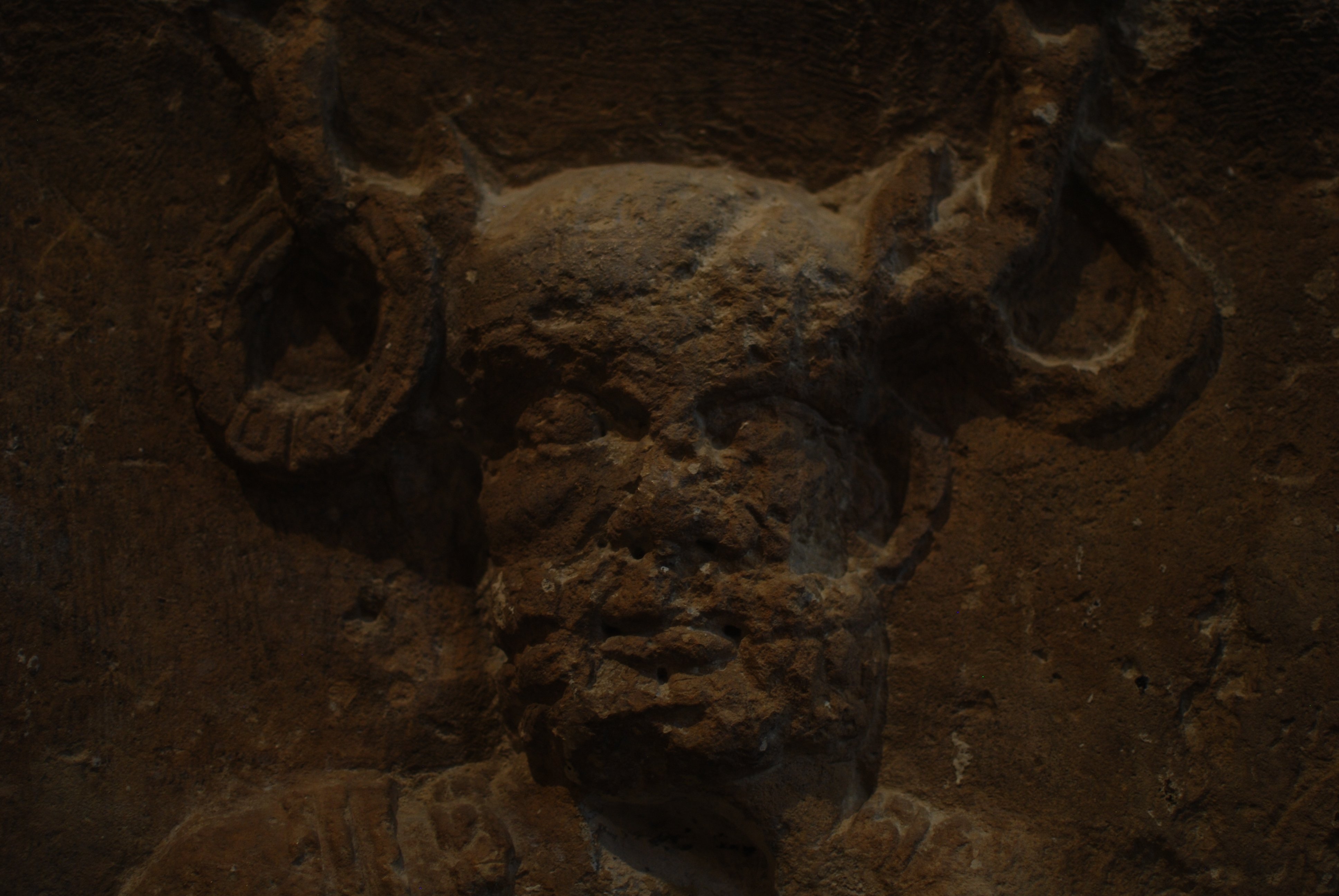 Bas-relief montrant une tête barbue surmontée par des bois, et de grands anneaux à la base de ses bois.
