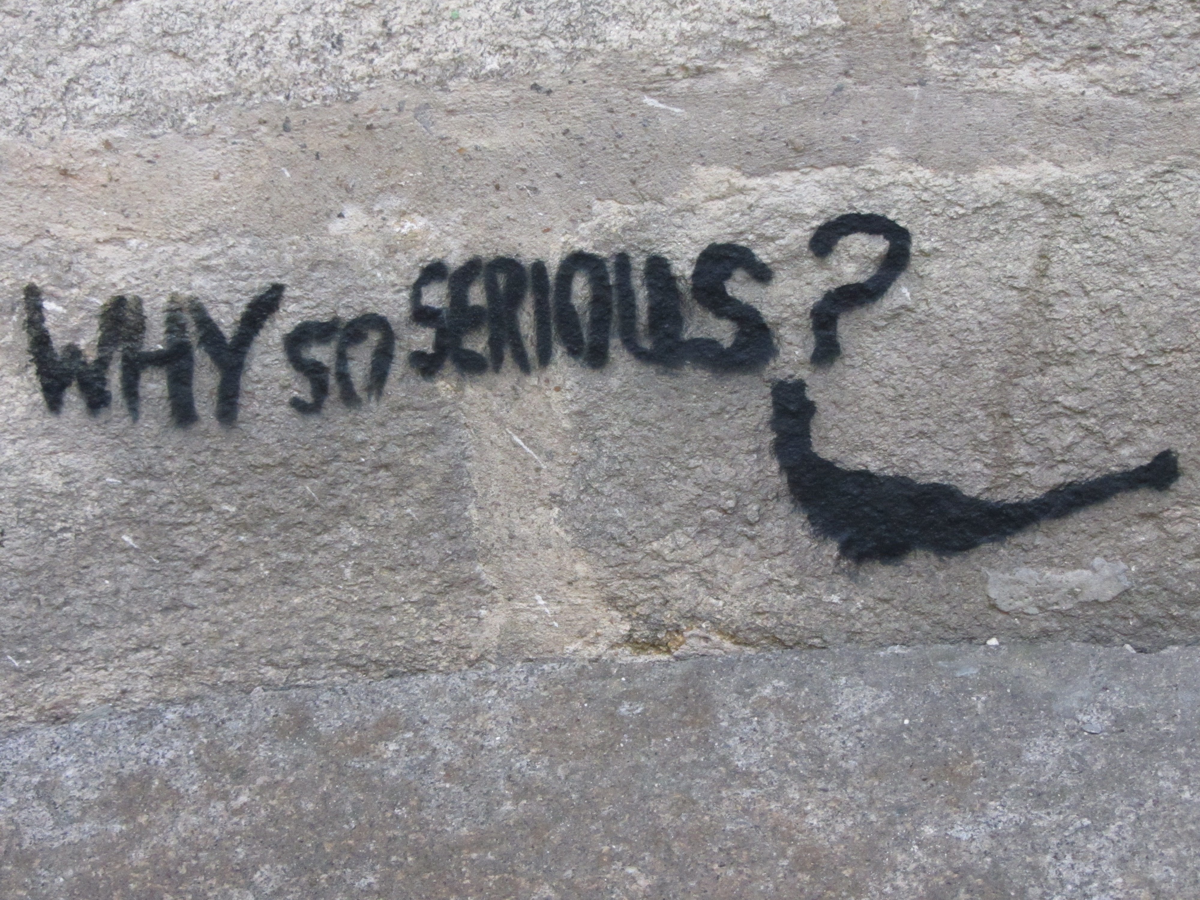 Mention "Why so serious?" avec un sourire taggué sur un mur en pierres