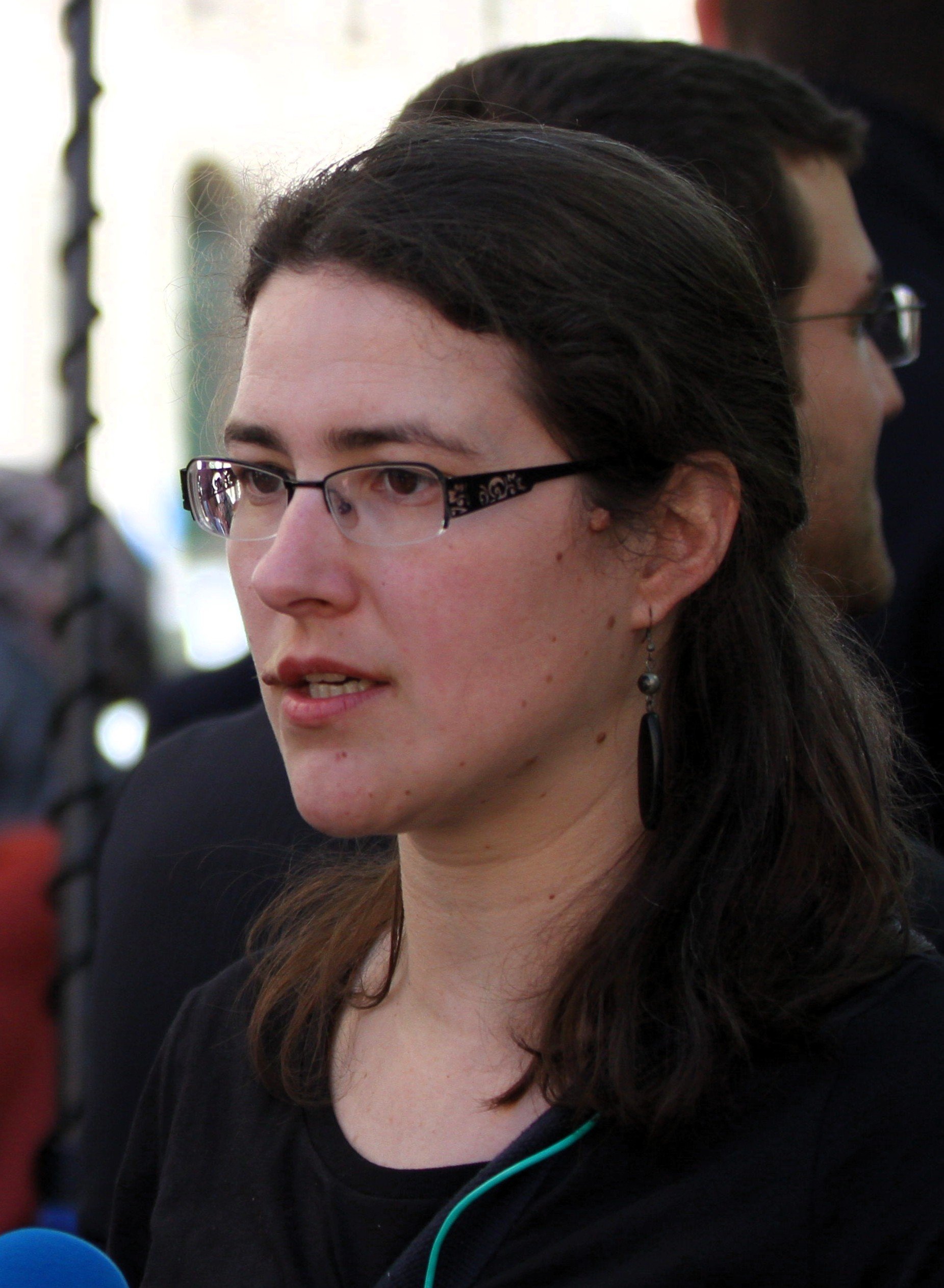 Portrait d’une jeune femme blanche avec de longs cheveux noirs et des lunettes à branches noires.