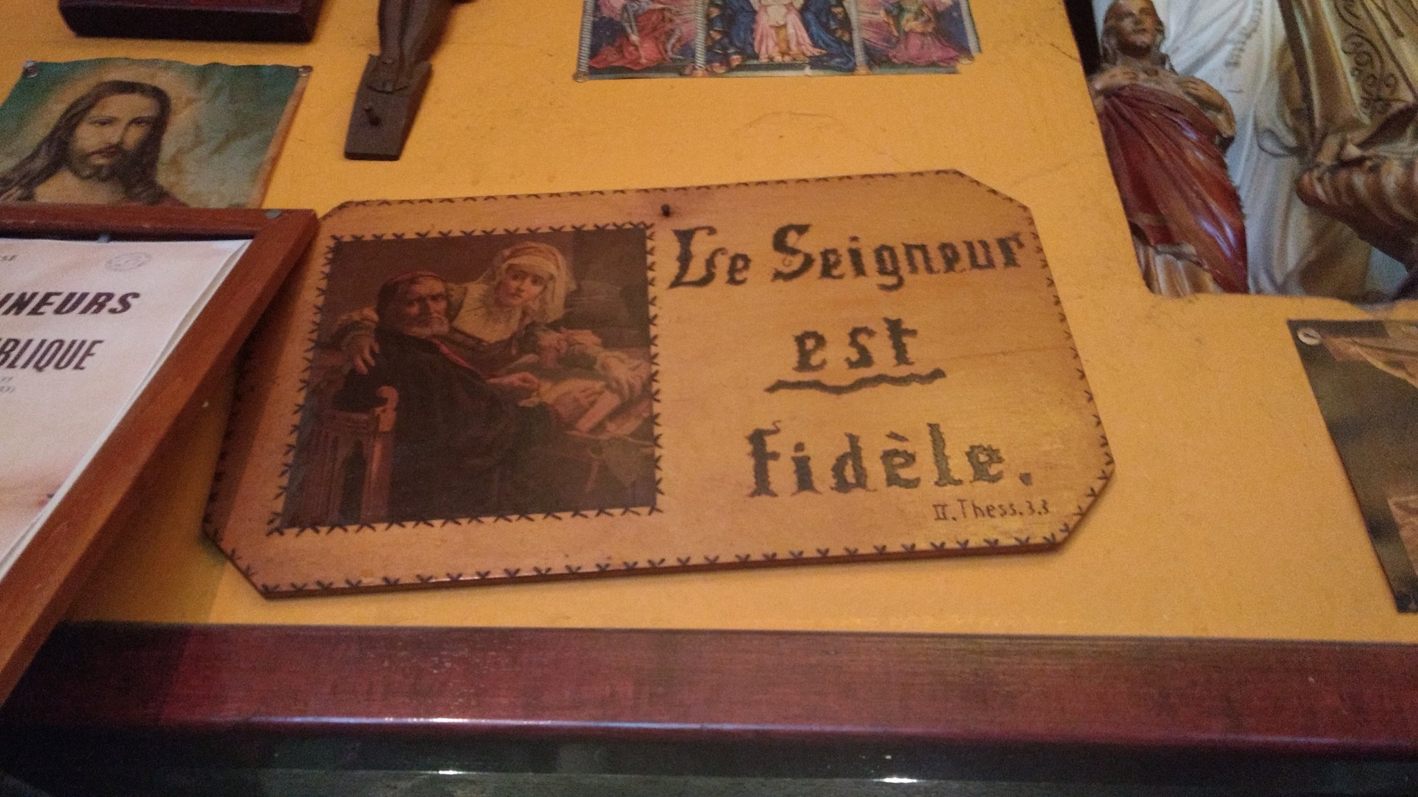 Photo d'un mur de bar couvert d'ex-votos un peu kitsch, centré sur un disant "Le Seigneur est fidèle - II. Thess. 3.3"