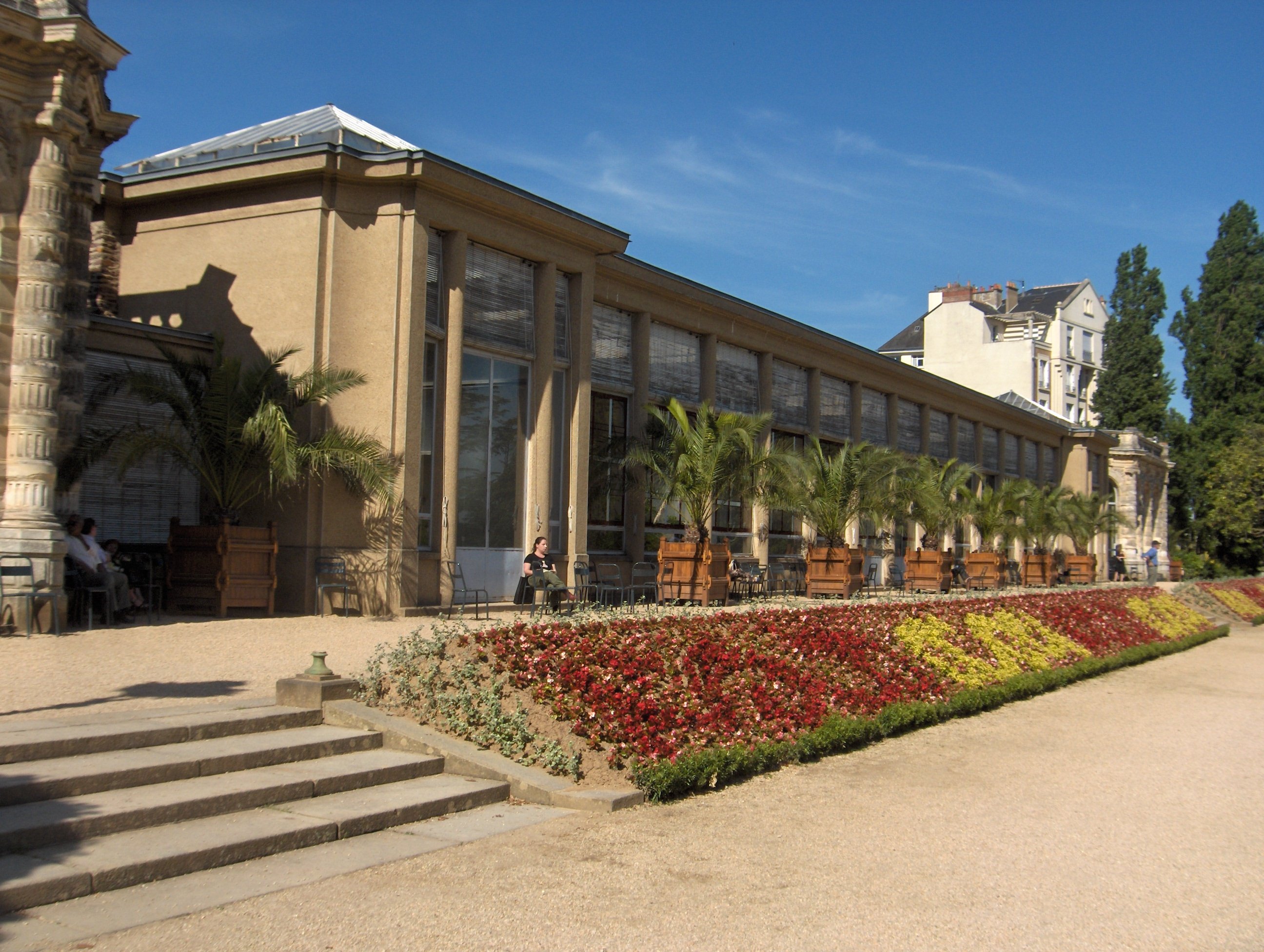 Un bâtiment classique, avec la façade entièrement vitrée. Entre cette façade et l'allée il y a un parterre de fleurs.