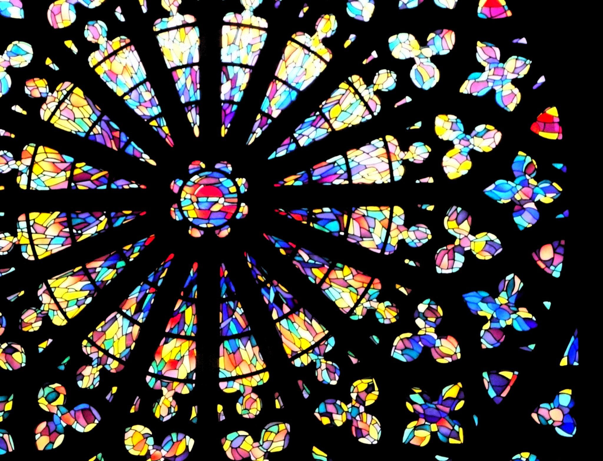 Photo d'un vitrail de type rosace d'une cathédrale gothique, où seul le verre est visible, la pierre étant noire.