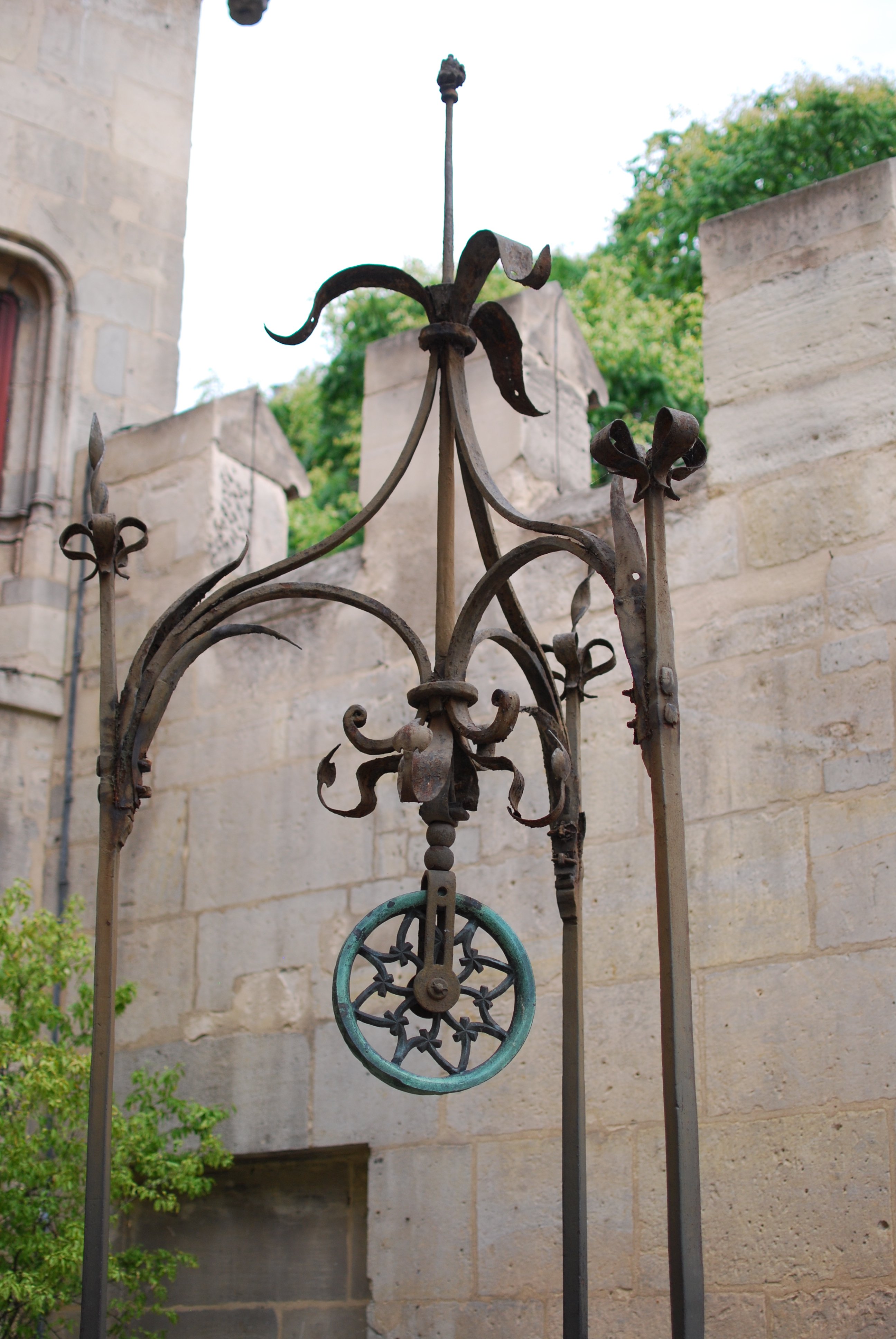 Une tête de puits en ferronnerie, avec une poulie couverte de vert-de-gris.