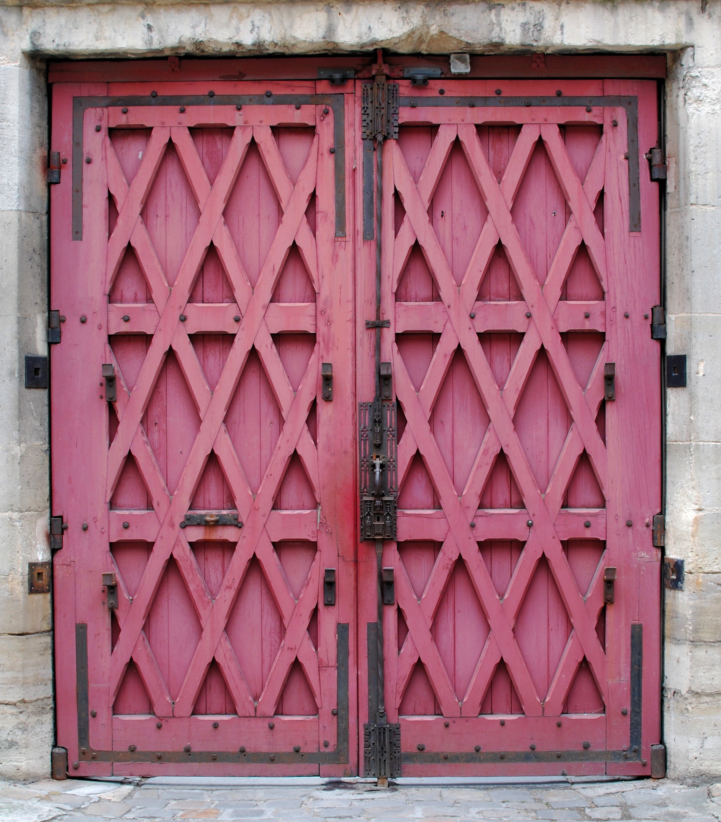 Une porte médiévale à deux battants, en bois rouges avec des renforts en croisillons et de la ferronnerie noire.